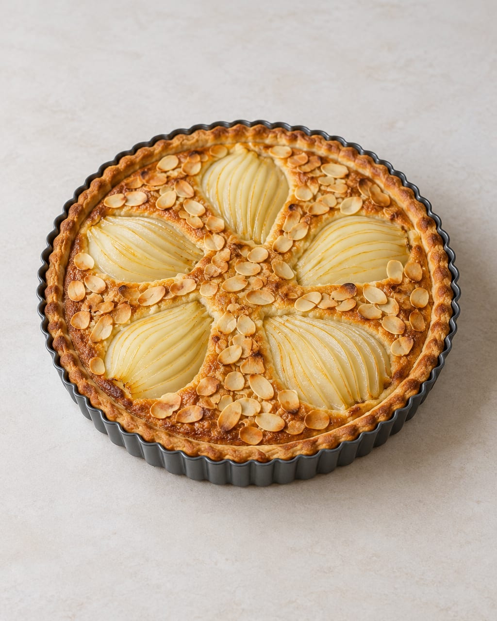 Tarte bourdaloue traditionnelle aux poires et amandes 2 Tarte bourdaloue dorée dans son moule, garnie de poires pochées en éventail et d’amandes effilées.